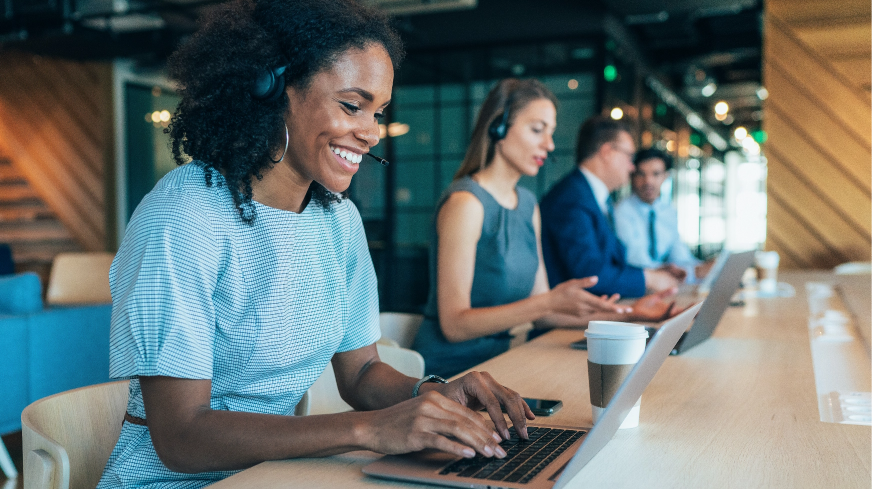 A worker chats helps a client over the phone. They sit at a laptop with a headset on to communicate