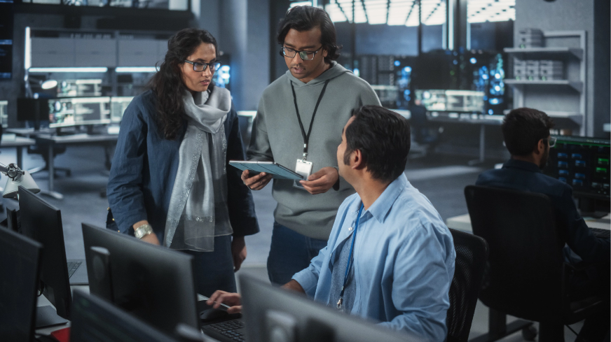 A team of three people talks through an issue at their desk