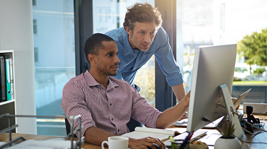 Two coworkers view information on a computer monitor