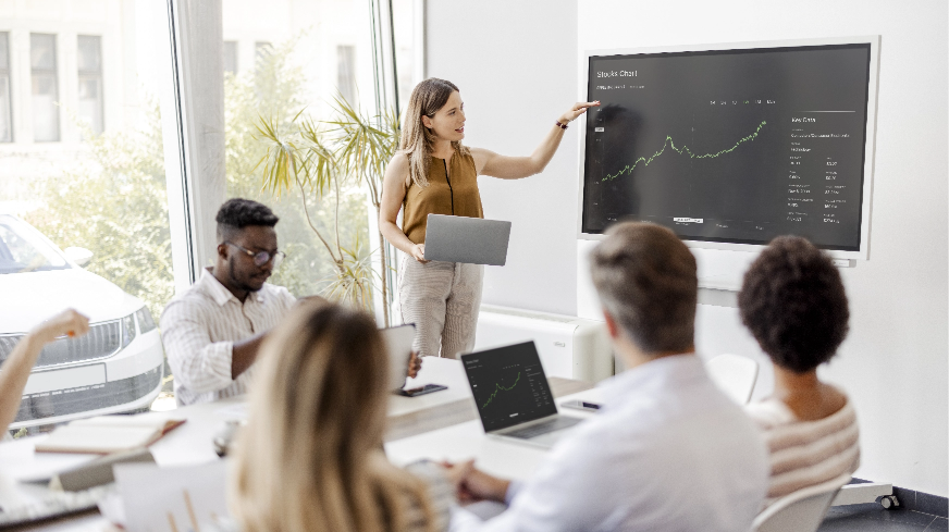 A business meeting with a present pointing at a graph showing increasing profits