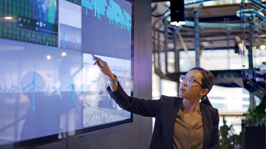 A business worker views multiple graphs and points to information on a large television display