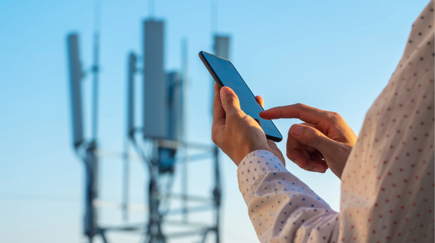 A person opens a cell phone call with a 5g tower in the visible background